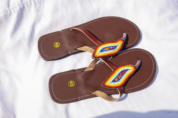A pair of brown sandals with an orange, yellow and red design.