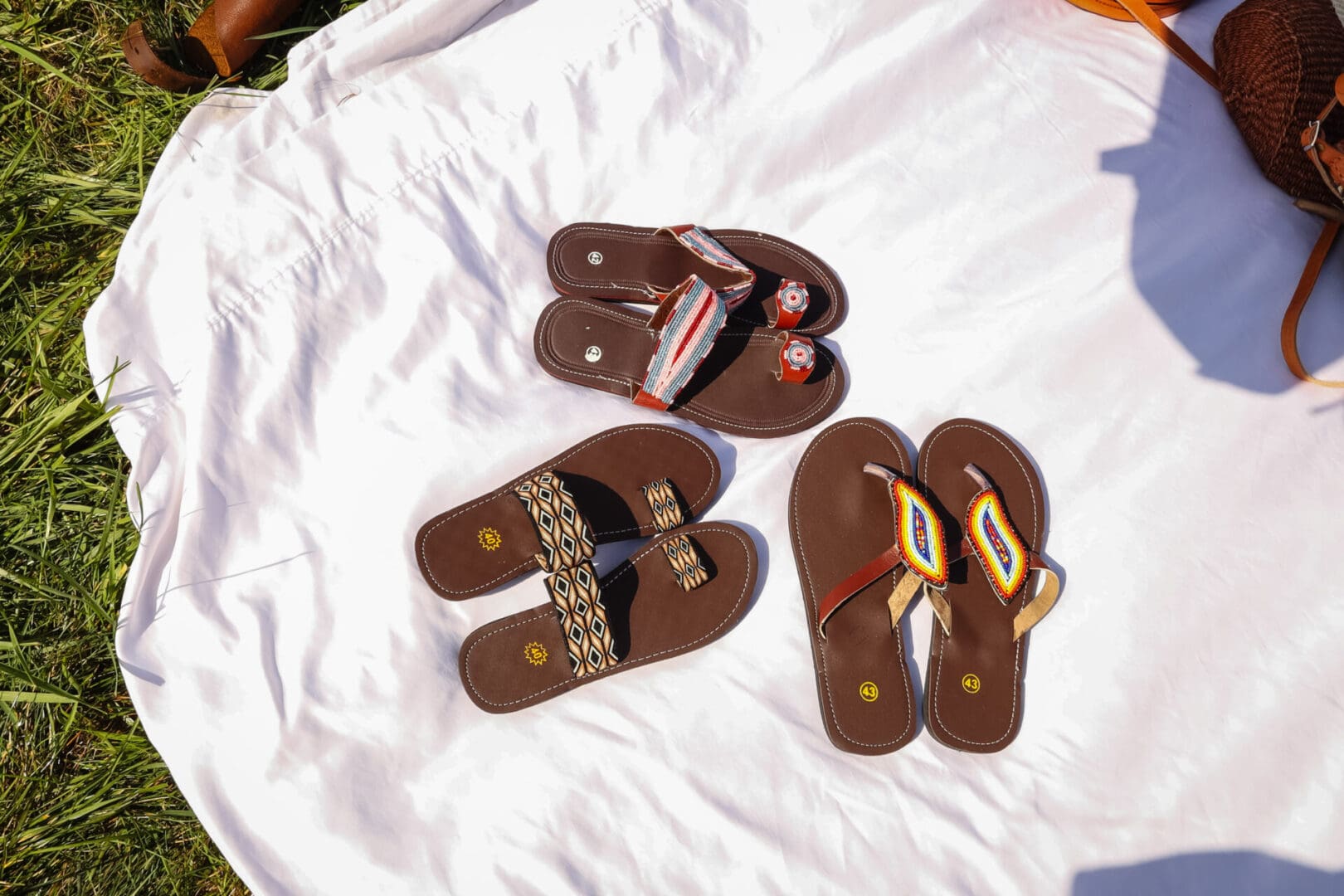 Three pairs of sandals are laying on a bed.
