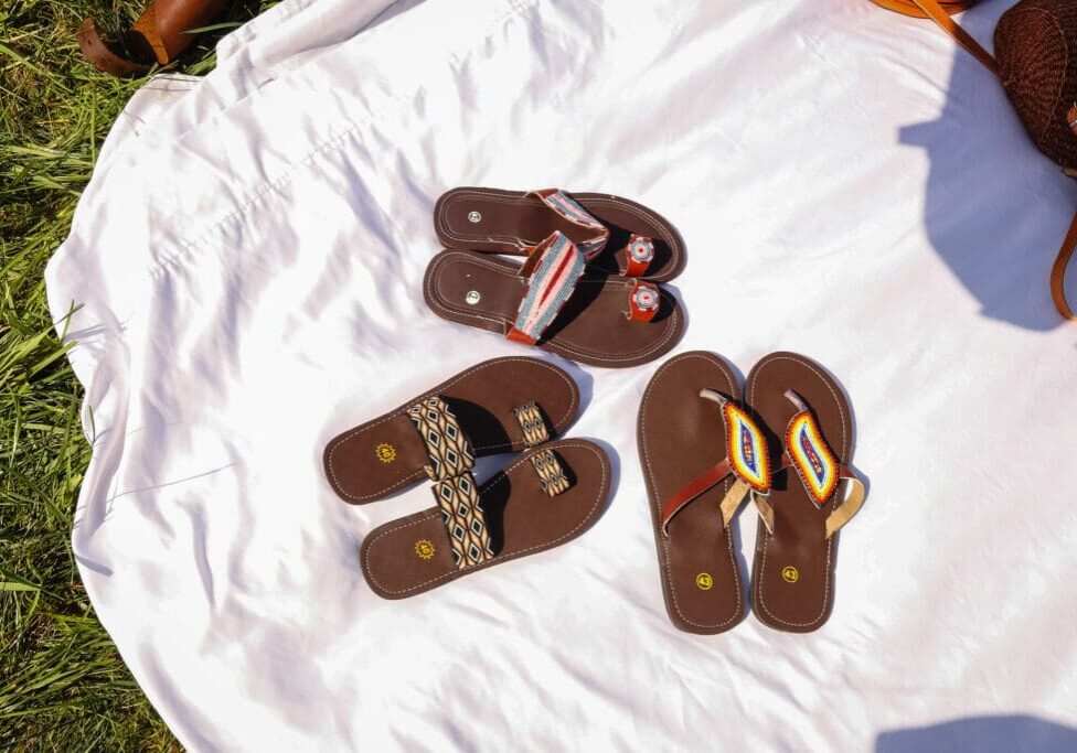 Three pairs of sandals are laying on a bed.